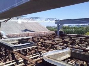 A high-angle view of a roof under construction, showing a metal frame structure, rafters, and rectangular vents.