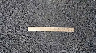 Wooden ruler lying horizontally on dark gravel ground.