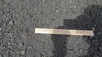 Ruler placed on dark gravel beside a concrete edge