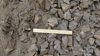 Wooden ruler lying on a pile of gray rocks and dirt