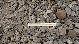 A pile of gray and brown gravel with a small wooden ruler laid across the center.