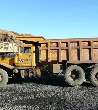 Yellow dump truck loaded with dirt on a gravel lot against a rocky hillside