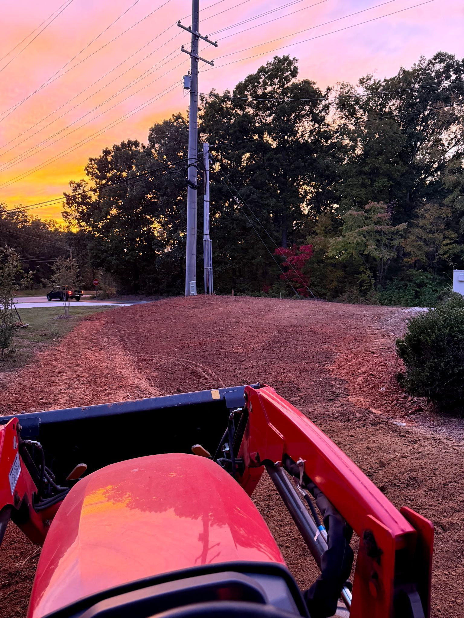 View from a red tractor driving along a gravel road at sunset, with trees and utility poles ahead