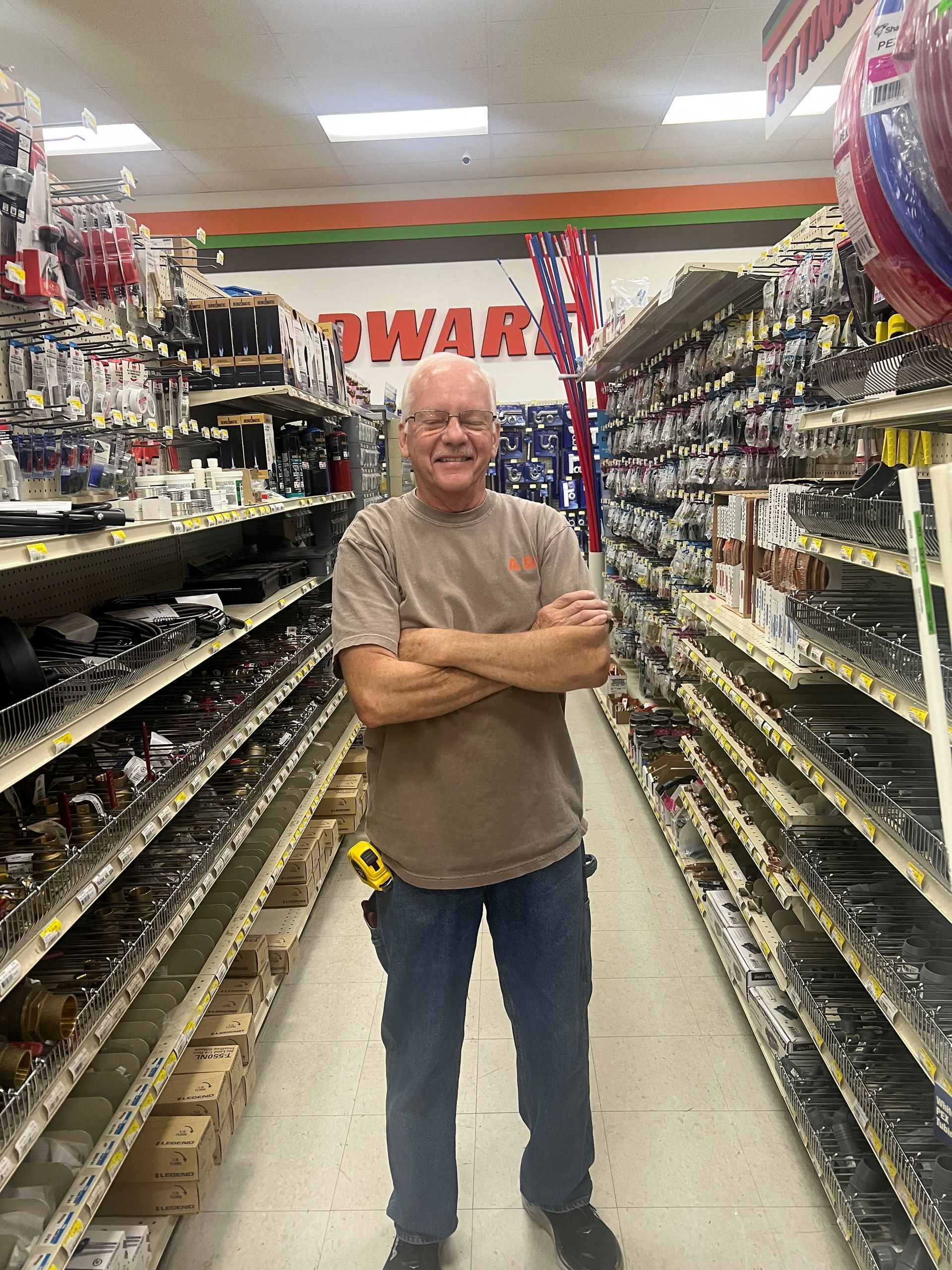 A man is standing in a hardware store with his arms crossed.