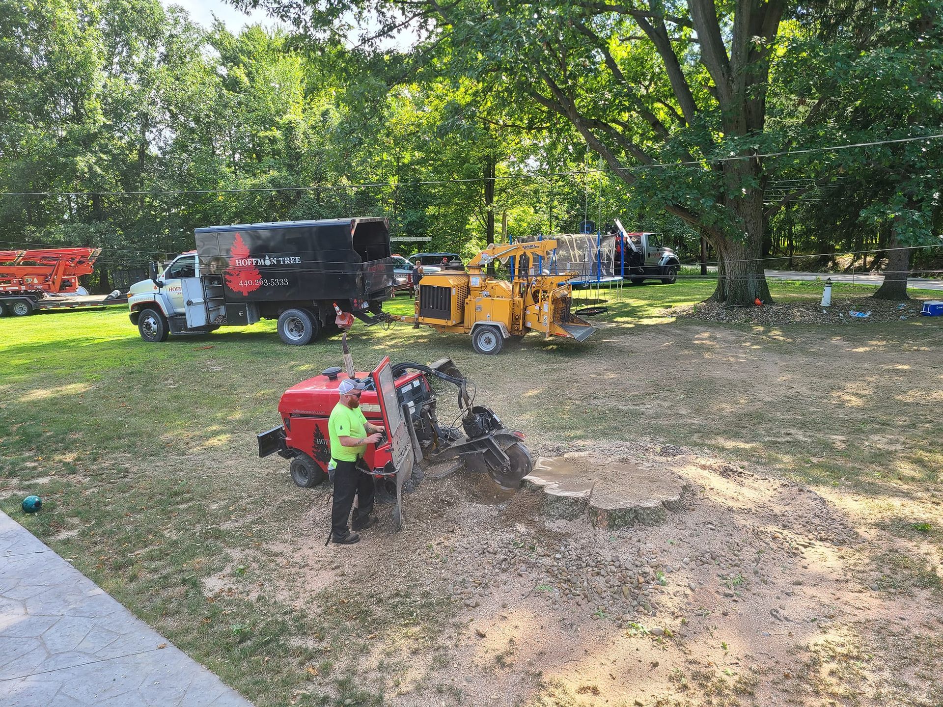A man is standing next to a stump grinder in a yard.