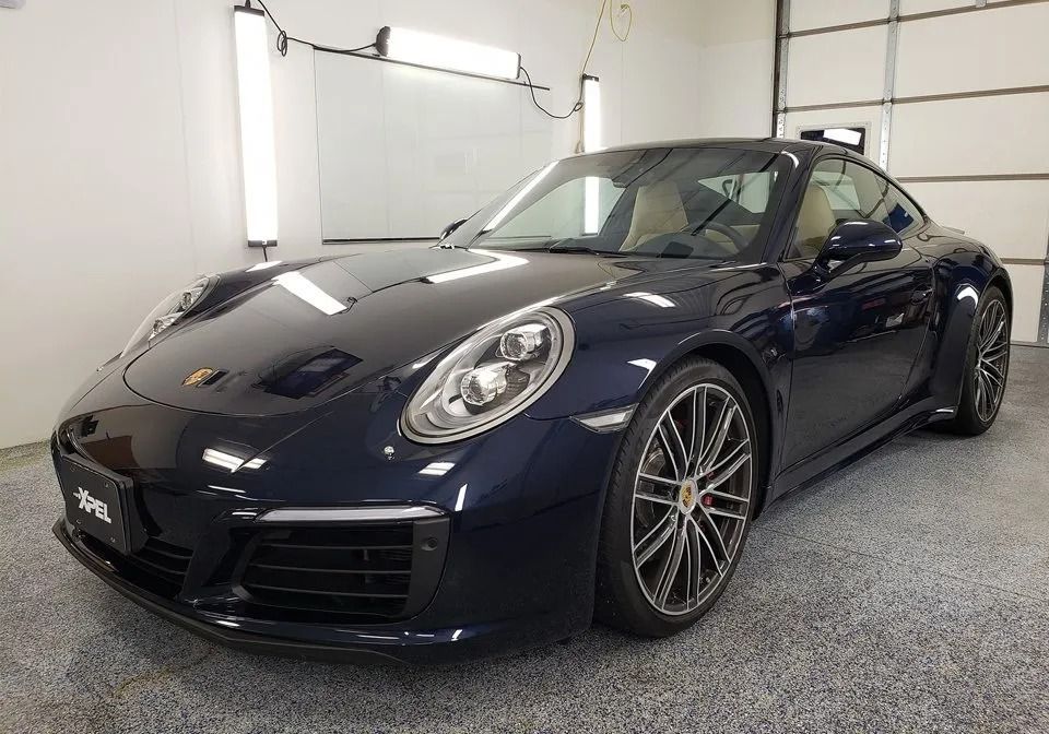 Dark blue Porsche 911 coupe in a well-lit garage, parked on a speckled floor.