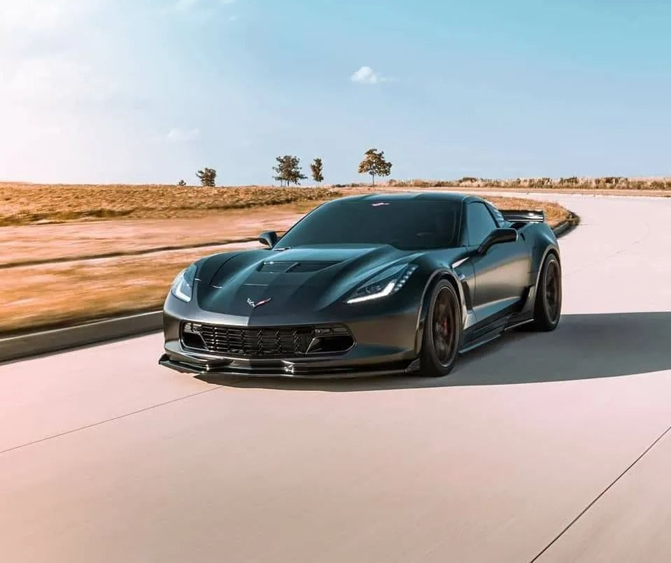 Dark gray sports car driving on a paved road, daytime.