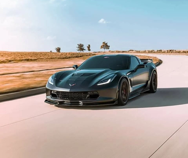Dark gray sports car driving on a paved road, daytime.