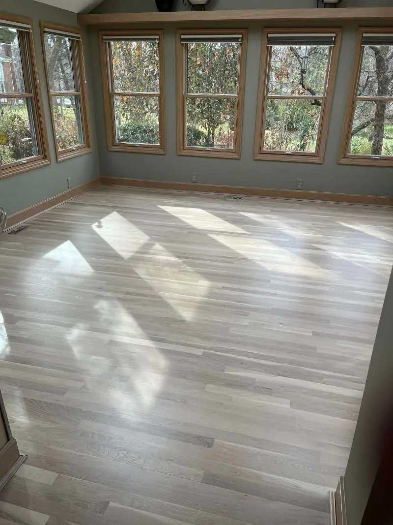 Sunroom with light wood floors, many windows, and neutral walls. Sunlight streams in.