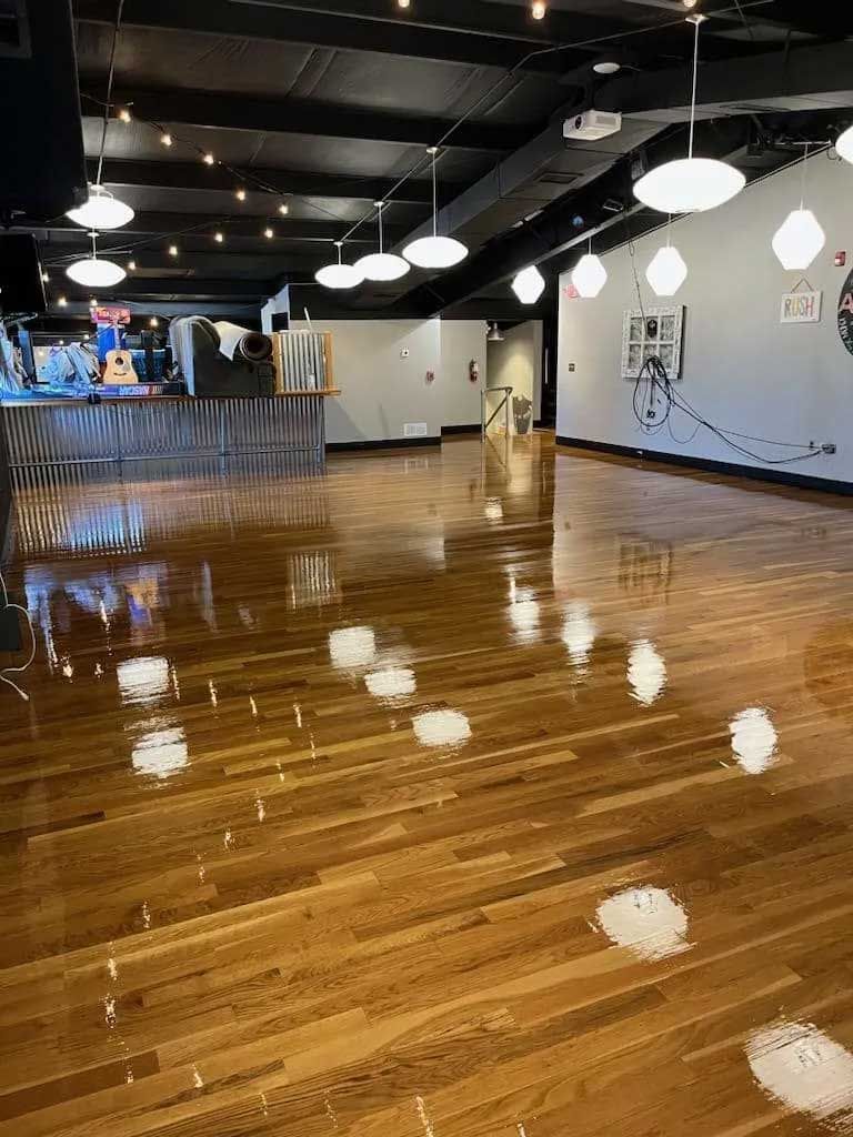 Empty wooden dance floor with overhead lights reflecting. Stage visible left.