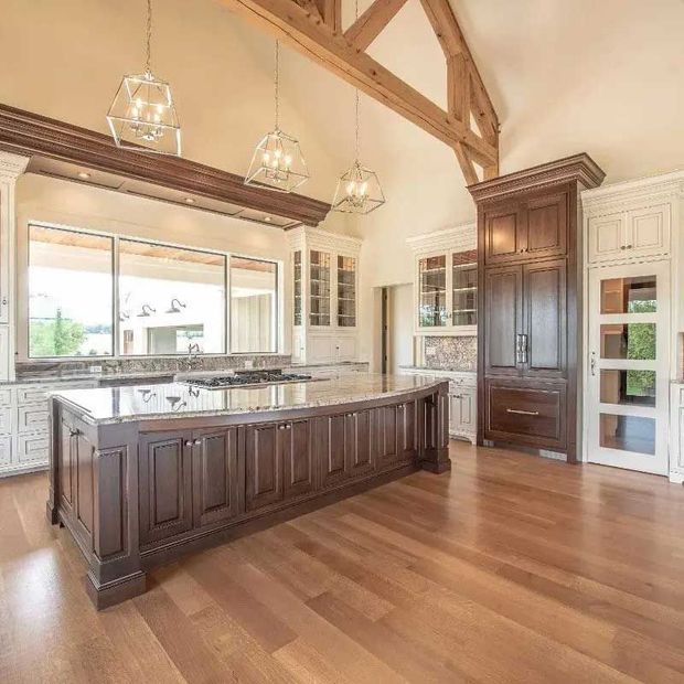 Spacious kitchen with large island, dark wood cabinets, light wood floor, and overhead beams.