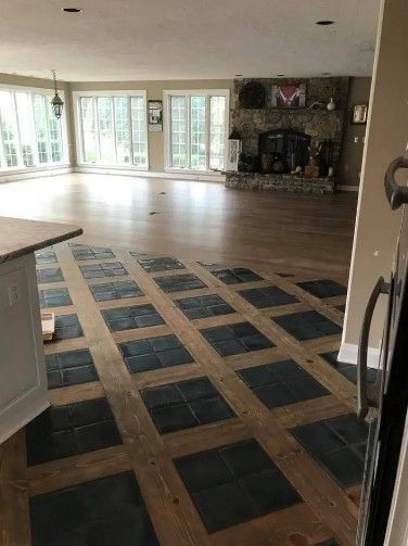Open-concept living space with partial wooden floor and tile pattern, stone fireplace, and large windows.