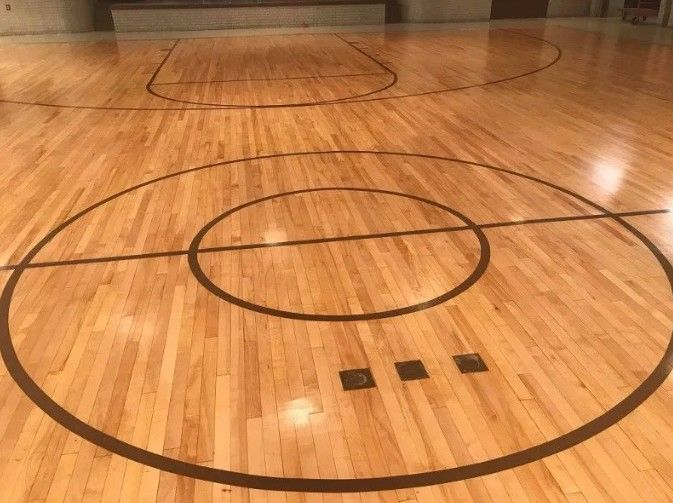 Wooden basketball court with black lines and center circle.