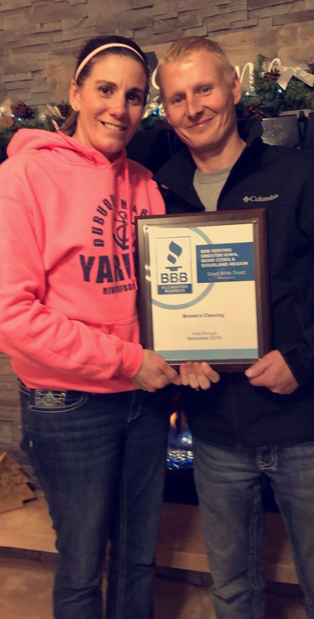 Two people smiling while holding a framed award plaque indoors