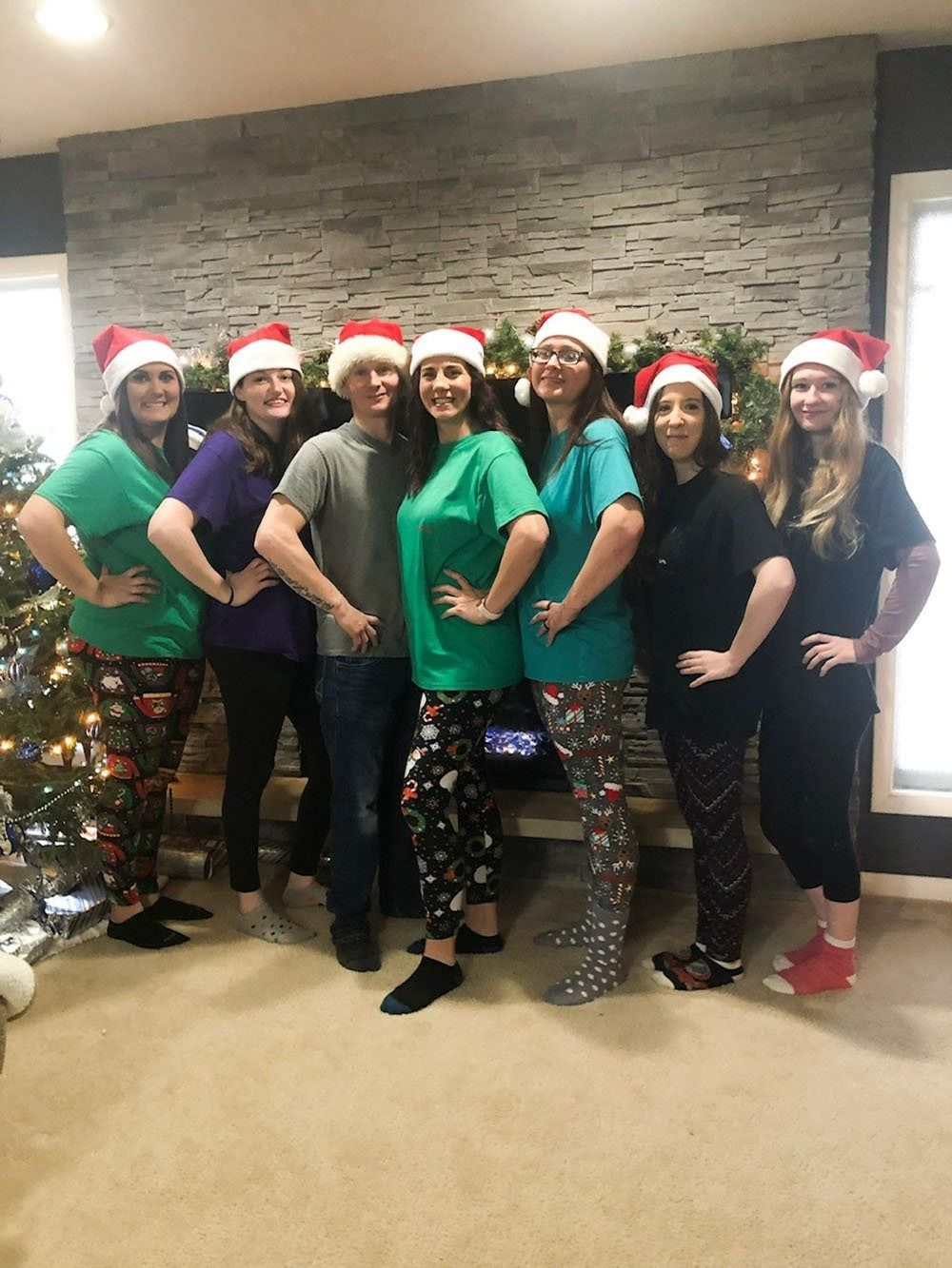 Group of coworkers in Santa hats and festive shirts posing together by a stone wall