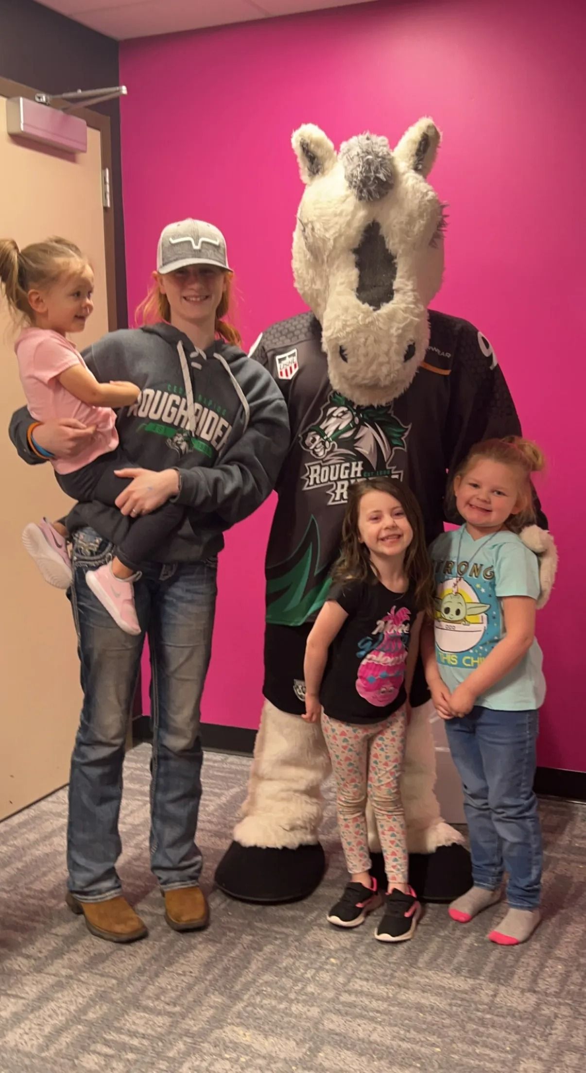 Family posing with a large horse mascot in front of a bright pink wall