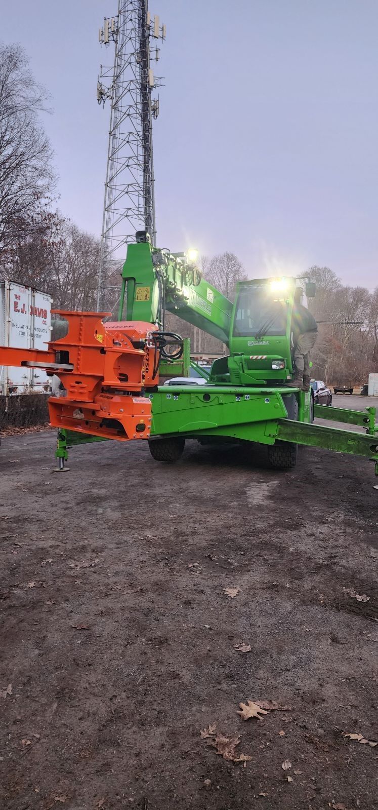 A green and orange crane is parked in a dirt lot.