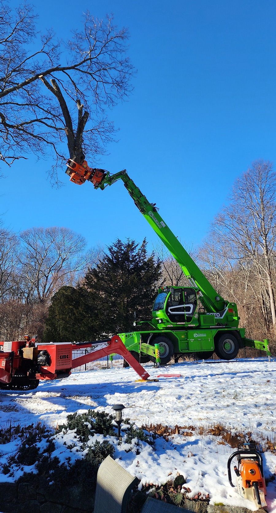 A green crane is cutting a tree in the snow.