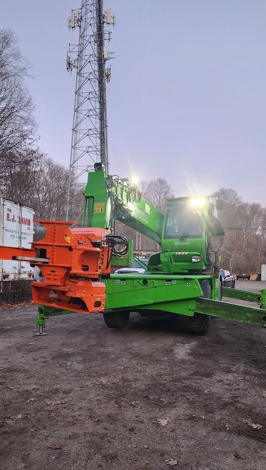 A green and orange crane is sitting in a parking lot next to a telephone pole.