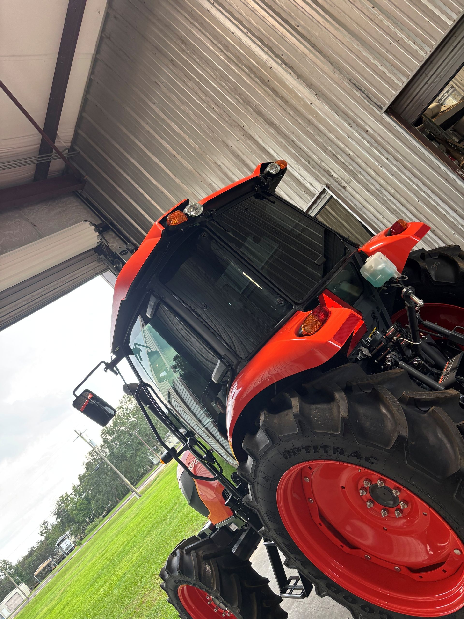 A bright orange tractor parked under a metal structure with a green grassy field visible in the background.