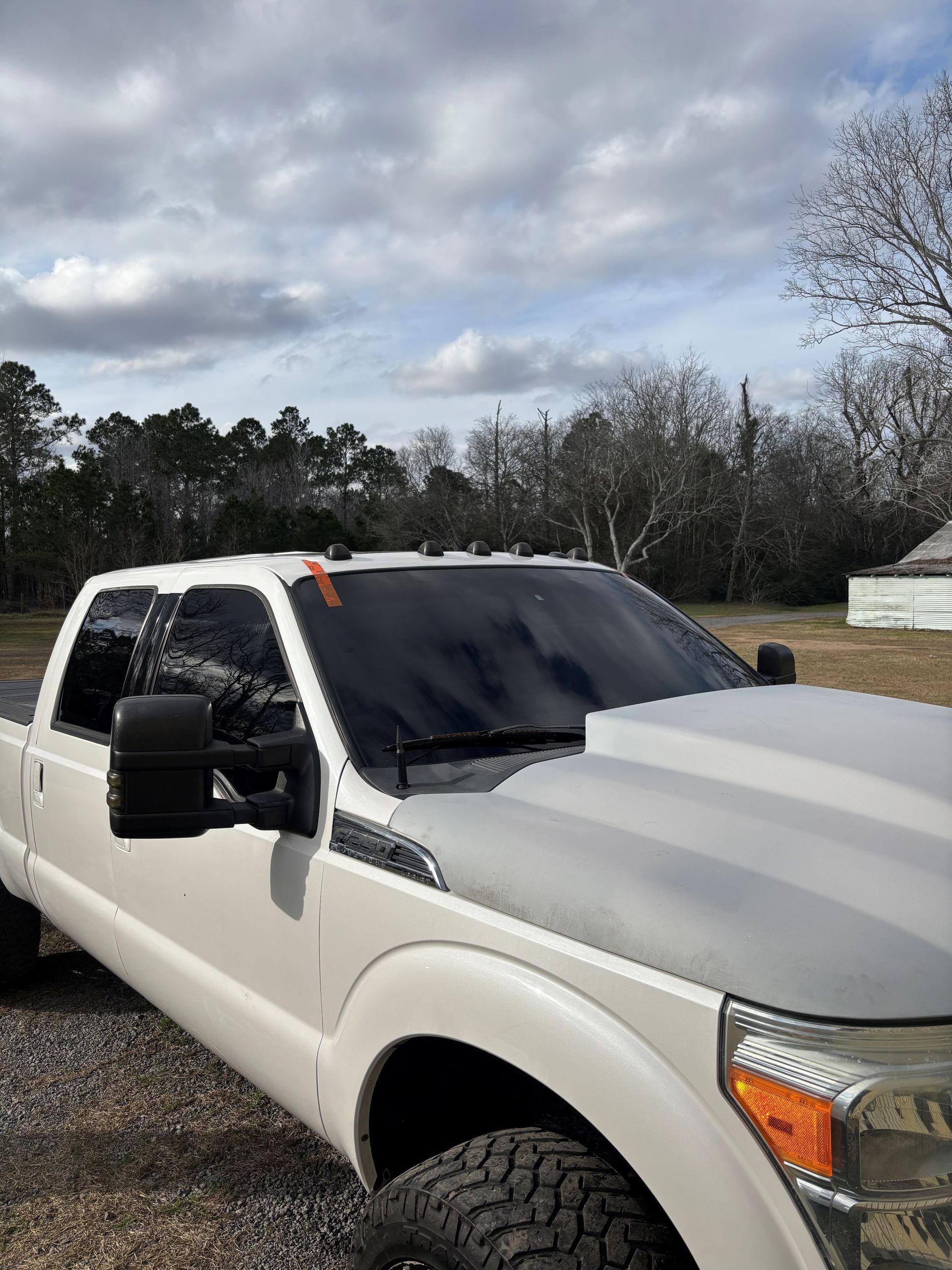 A white pickup truck with a gray aftermarket hood and dark tinted windshield parked outdoors.