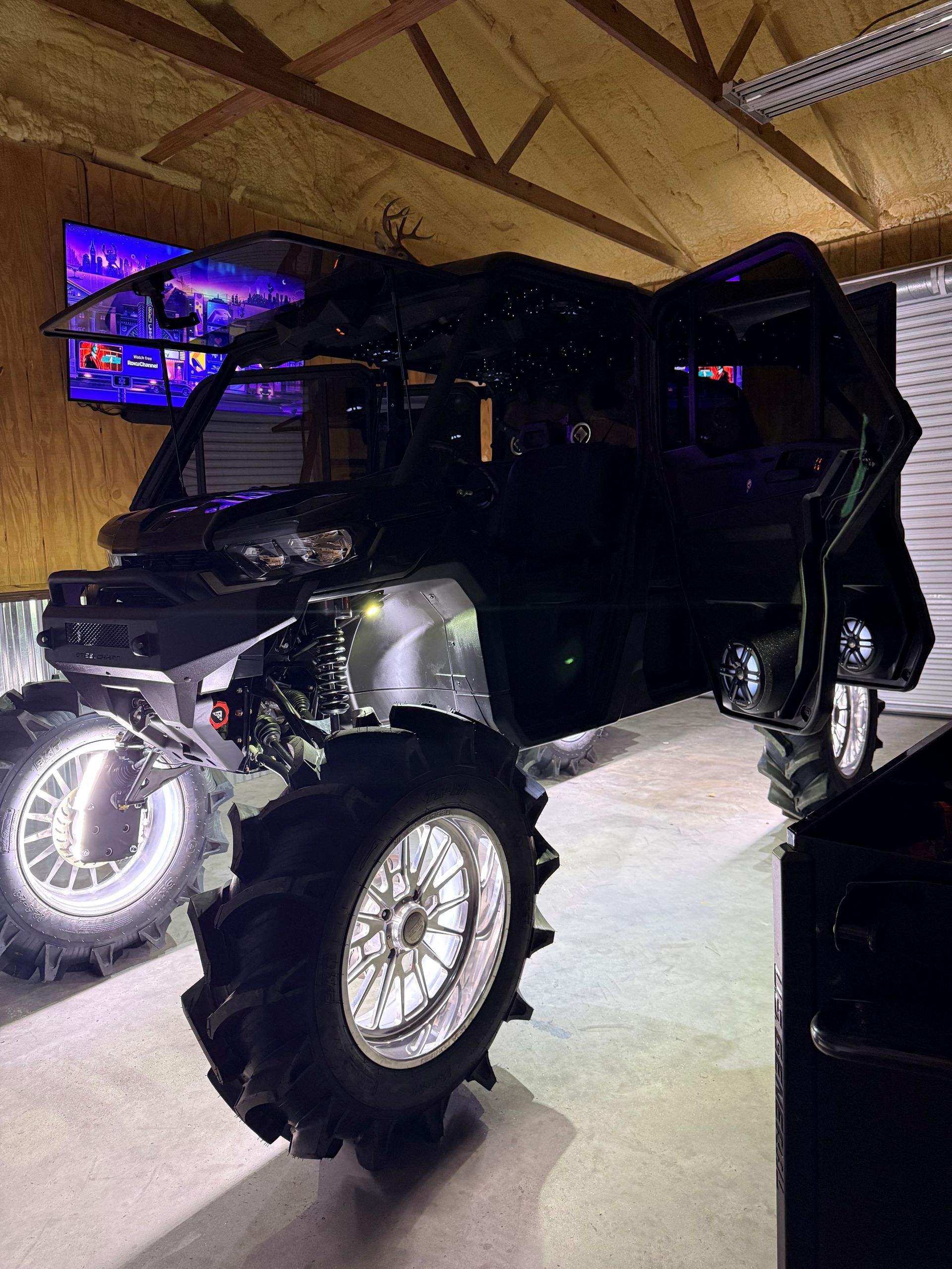 A black side-by-side off-road vehicle with large, deep-tread tires and bright glowing rims parked inside a garage.