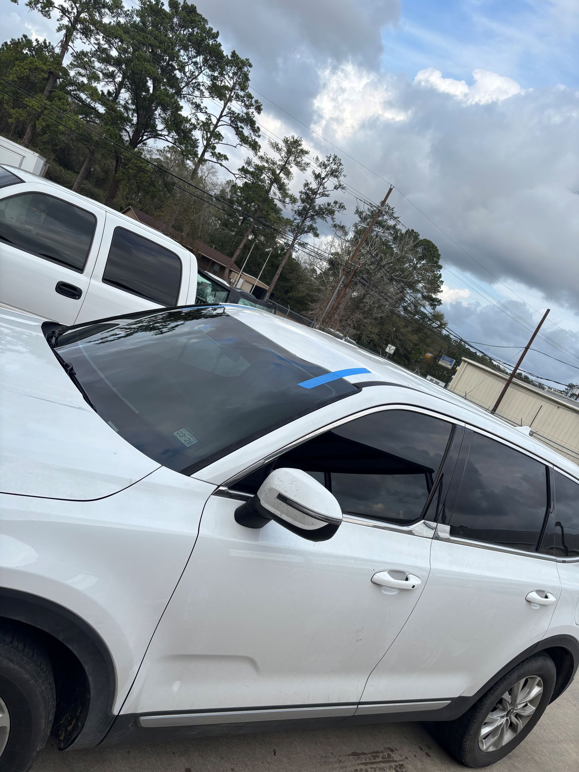 A white SUV parked outdoors with a blue piece of tape centered on the top of the windshield.