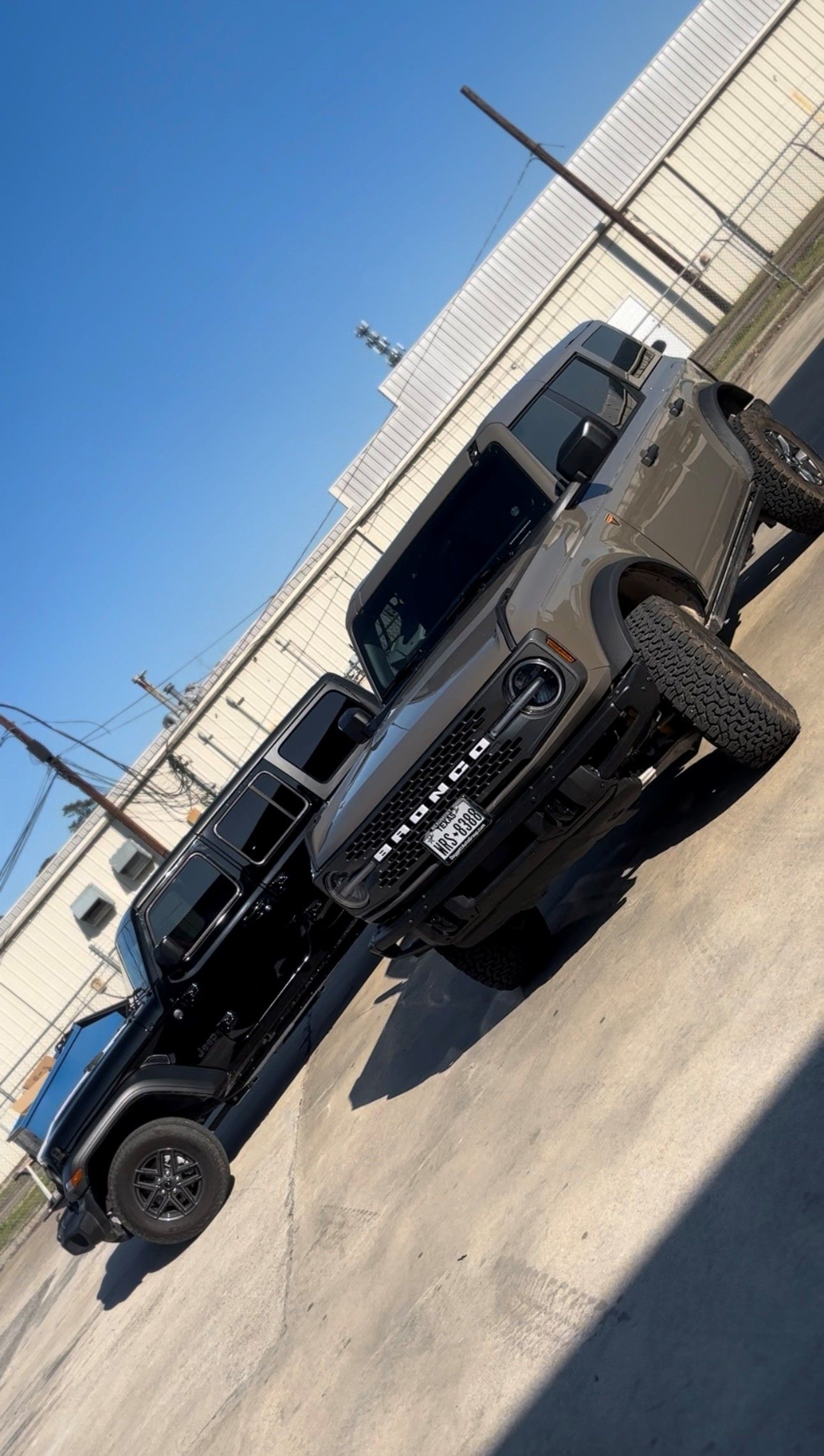 Two black Ford Bronco SUVs parked side-by-side on an asphalt lot under a clear blue sky.
