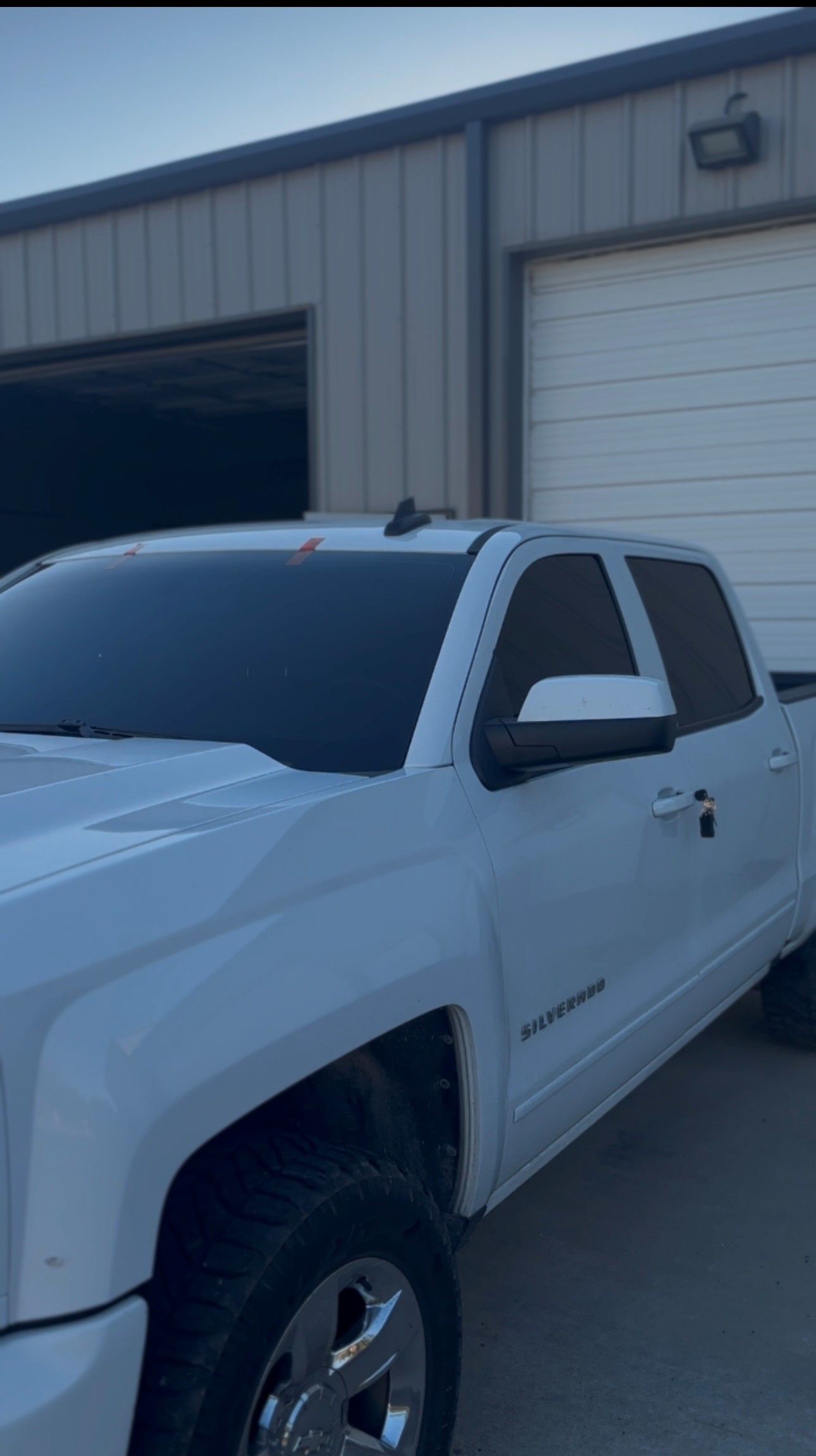 A white pickup truck with tinted windows parked in front of a metal industrial building.