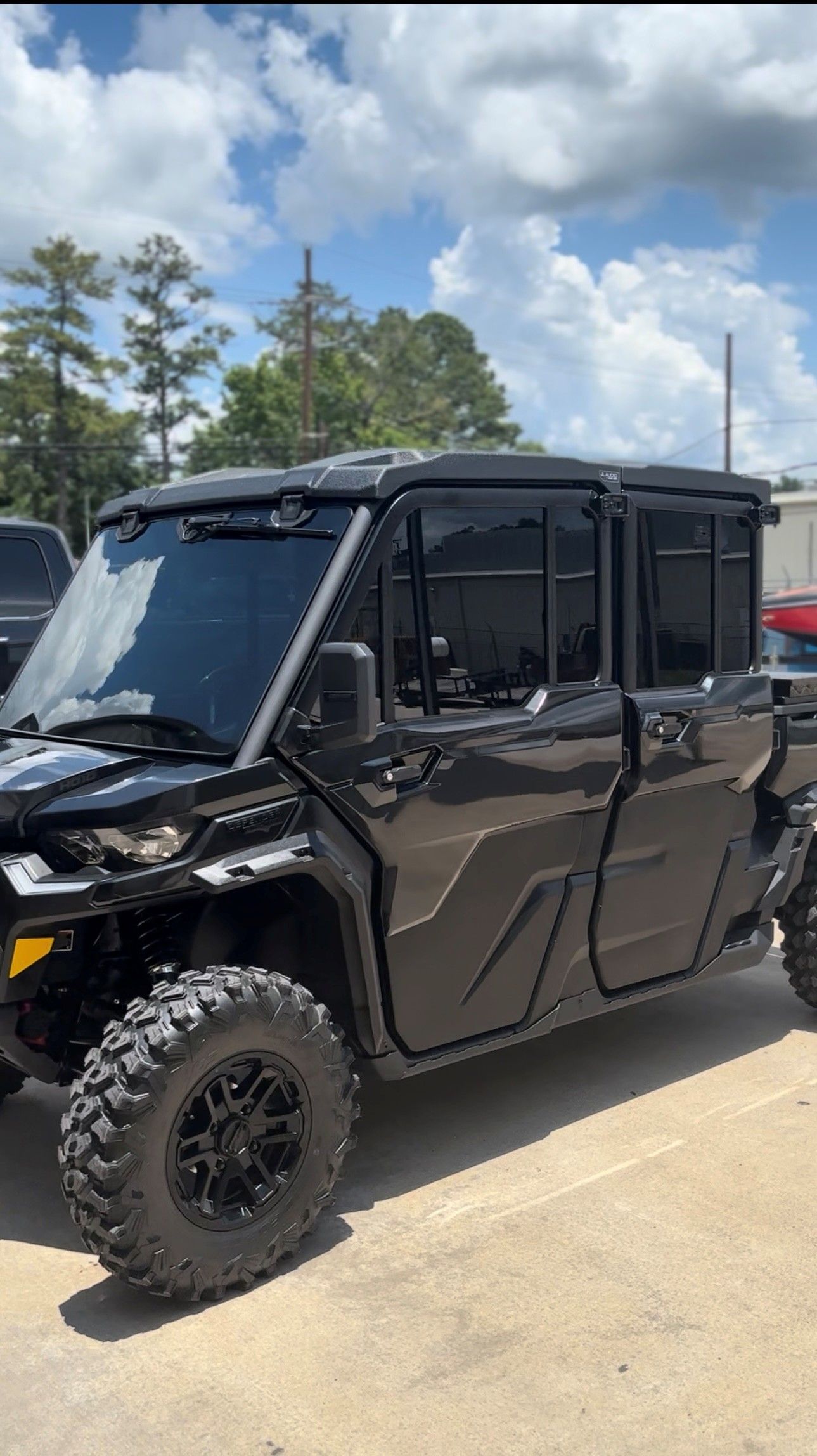 A black, four-door side-by-side utility vehicle with rugged off-road tires, parked outdoors on a paved lot.