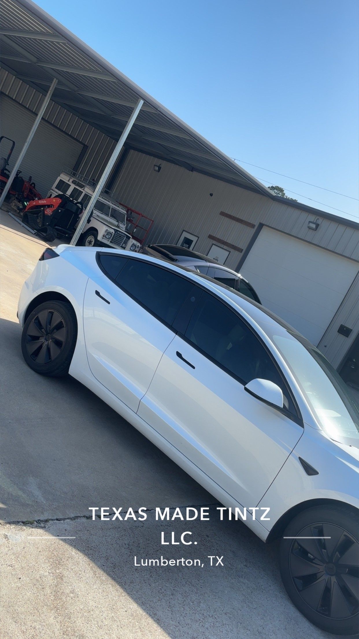 A white Tesla parked outside an industrial building with a Texas Made Tintz LLC watermark overlay.