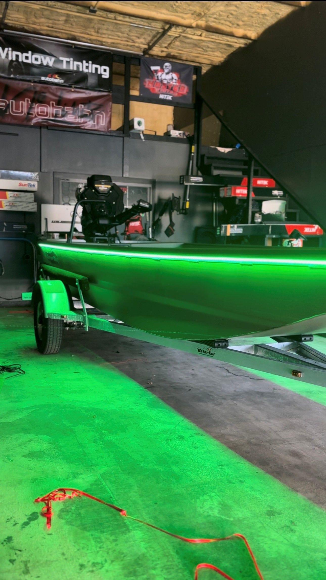 A boat on a trailer in a shop, illuminated by vibrant green LED lights along its side and reflecting on the ground.