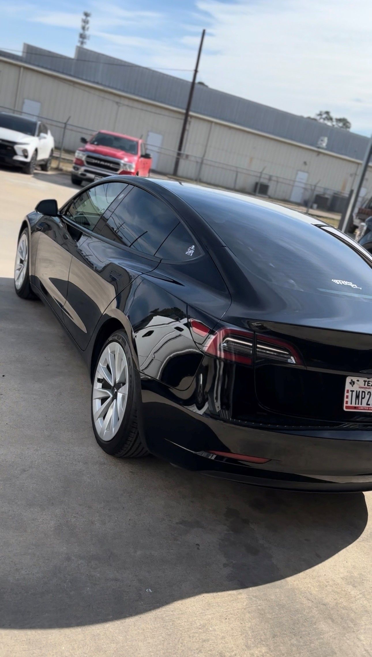 A black Tesla Model 3 parked in an outdoor lot on a sunny day.