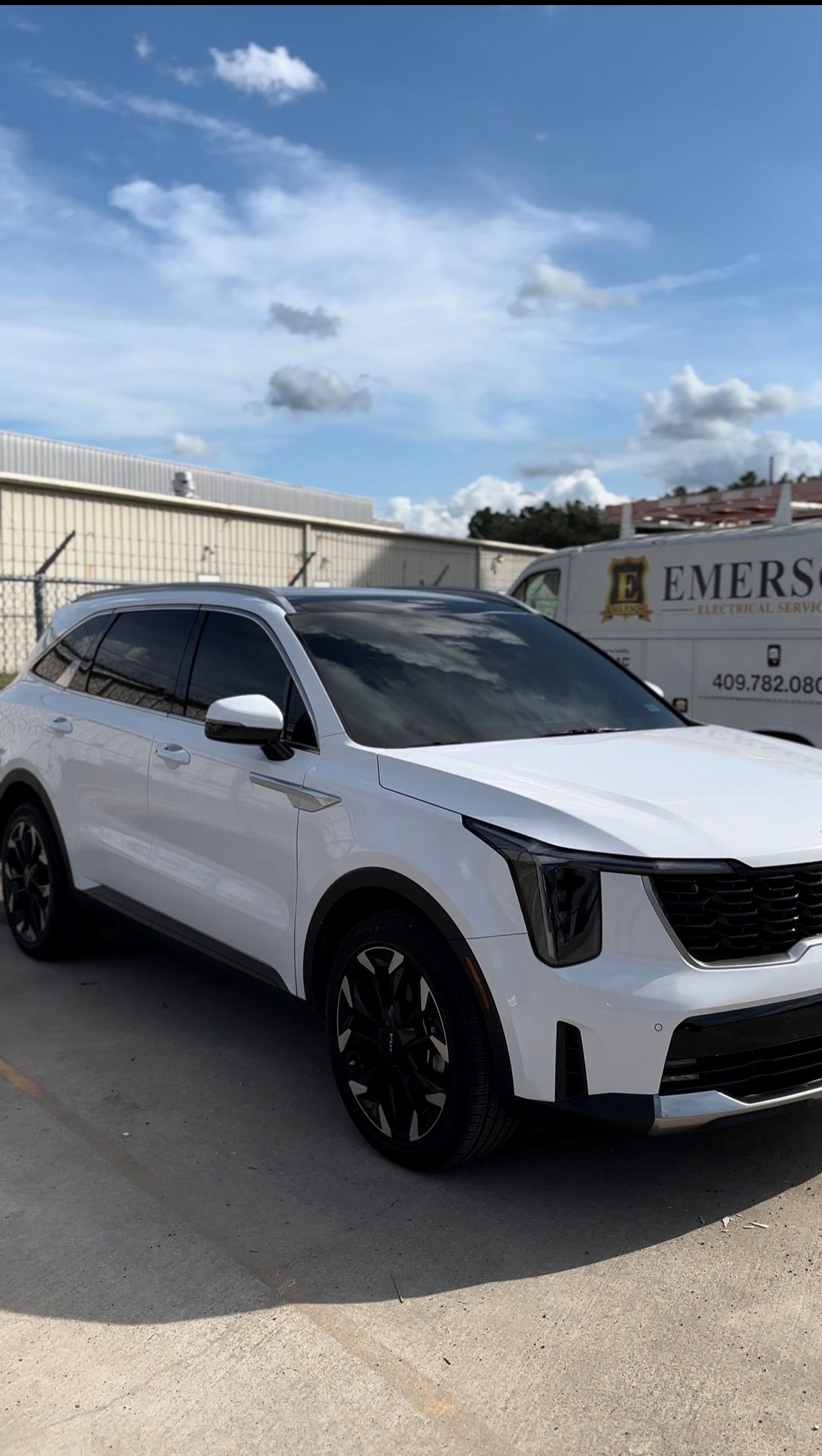 A white Cadillac XT6 SUV with black rims parked in a paved lot under a blue sky with clouds.