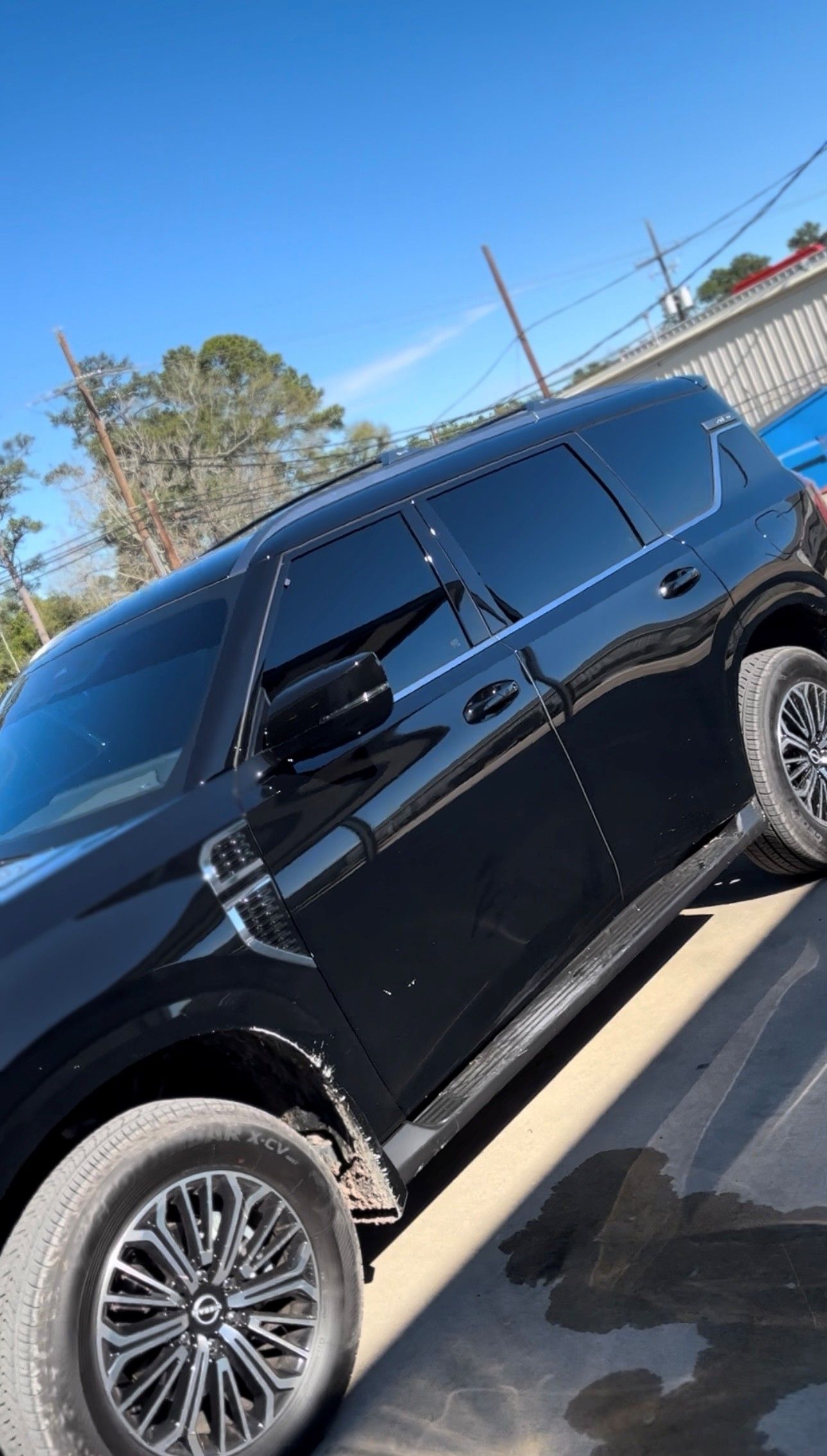 A black SUV parked on an asphalt surface under a clear blue sky, viewed from a high angle.