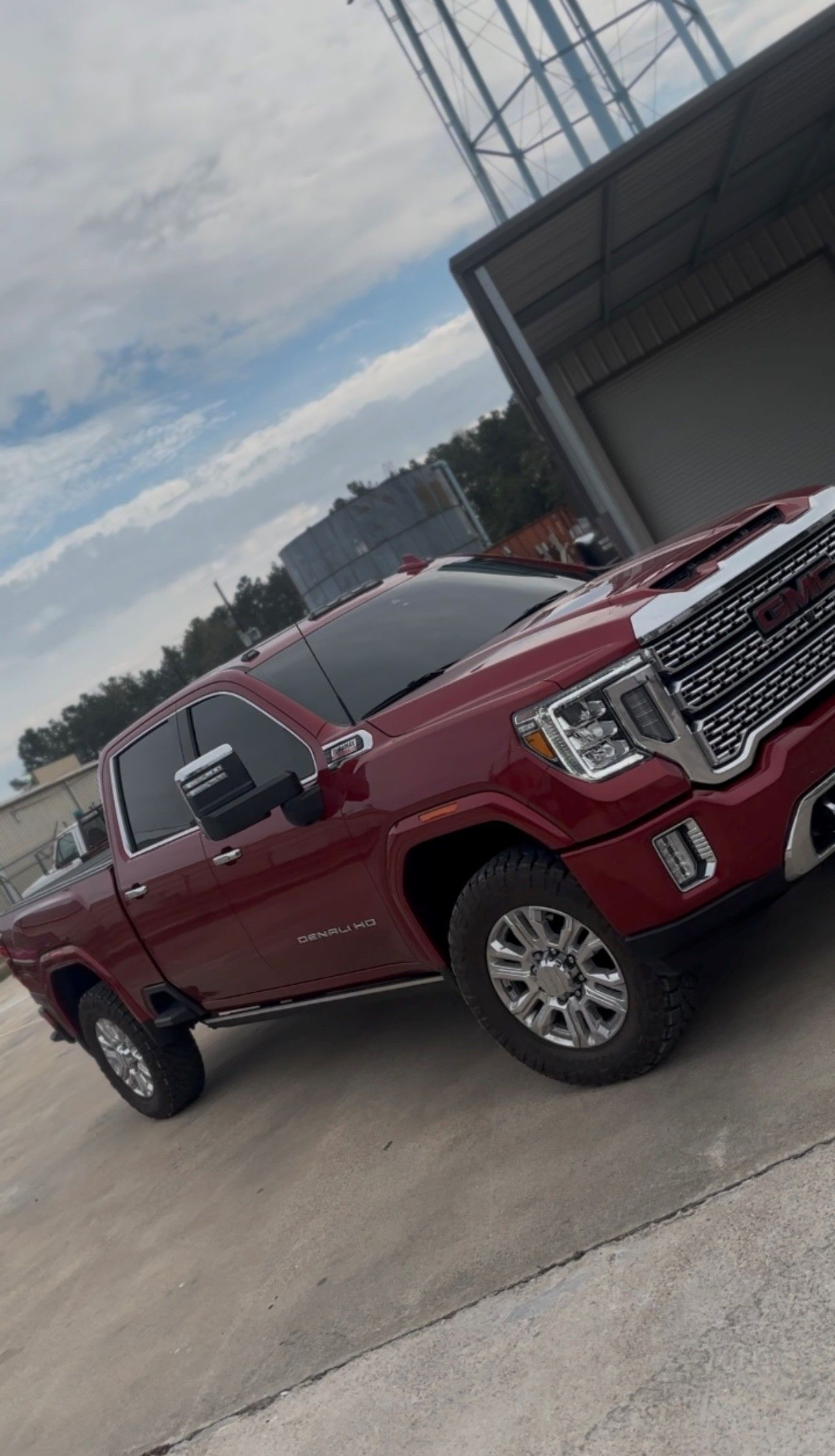A maroon GMC Sierra Denali crew cab pickup truck parked on a concrete lot near a water tower.