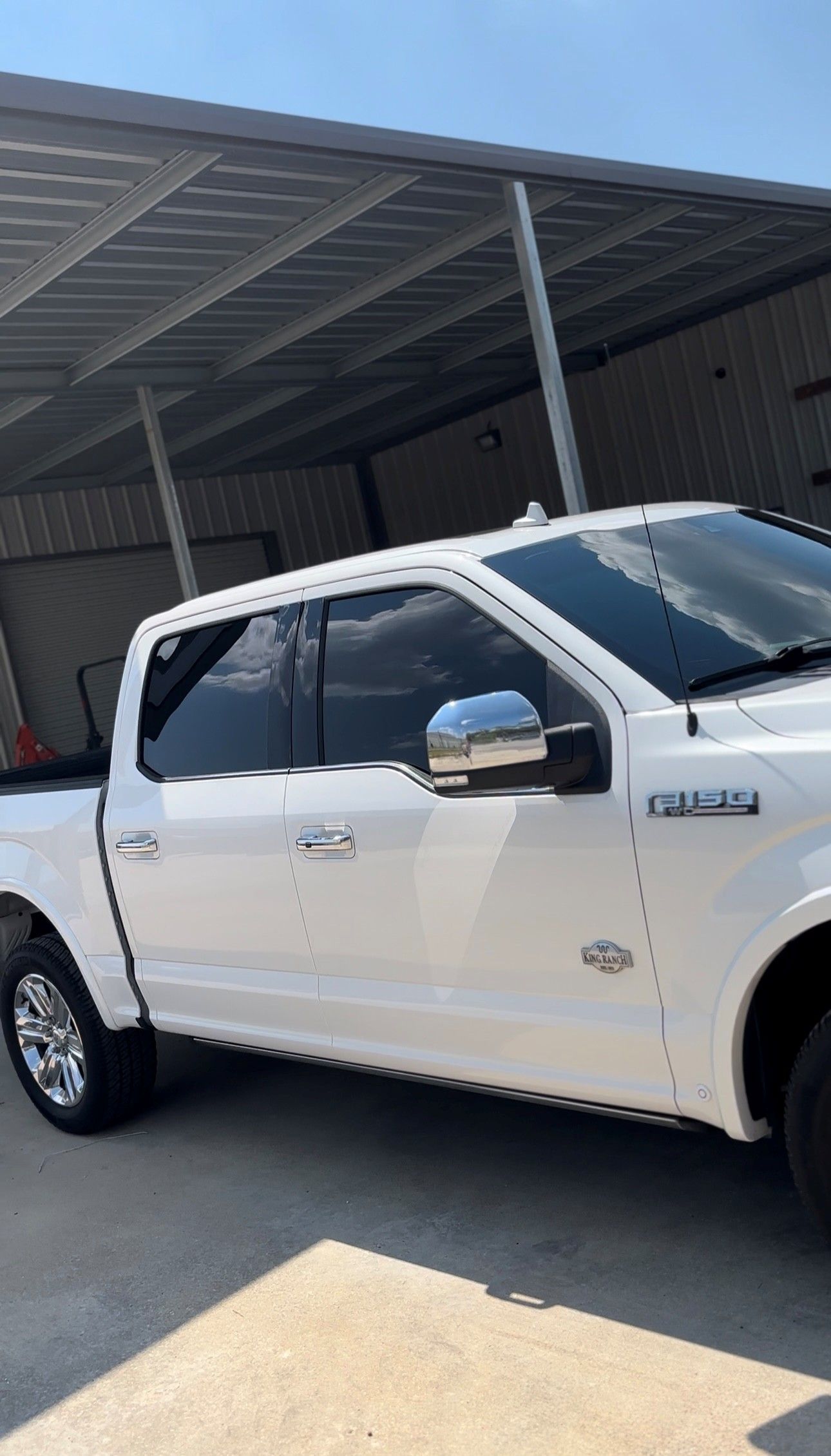A white Ford F-150 crew cab pickup truck parked under a metal carport on a sunny day.
