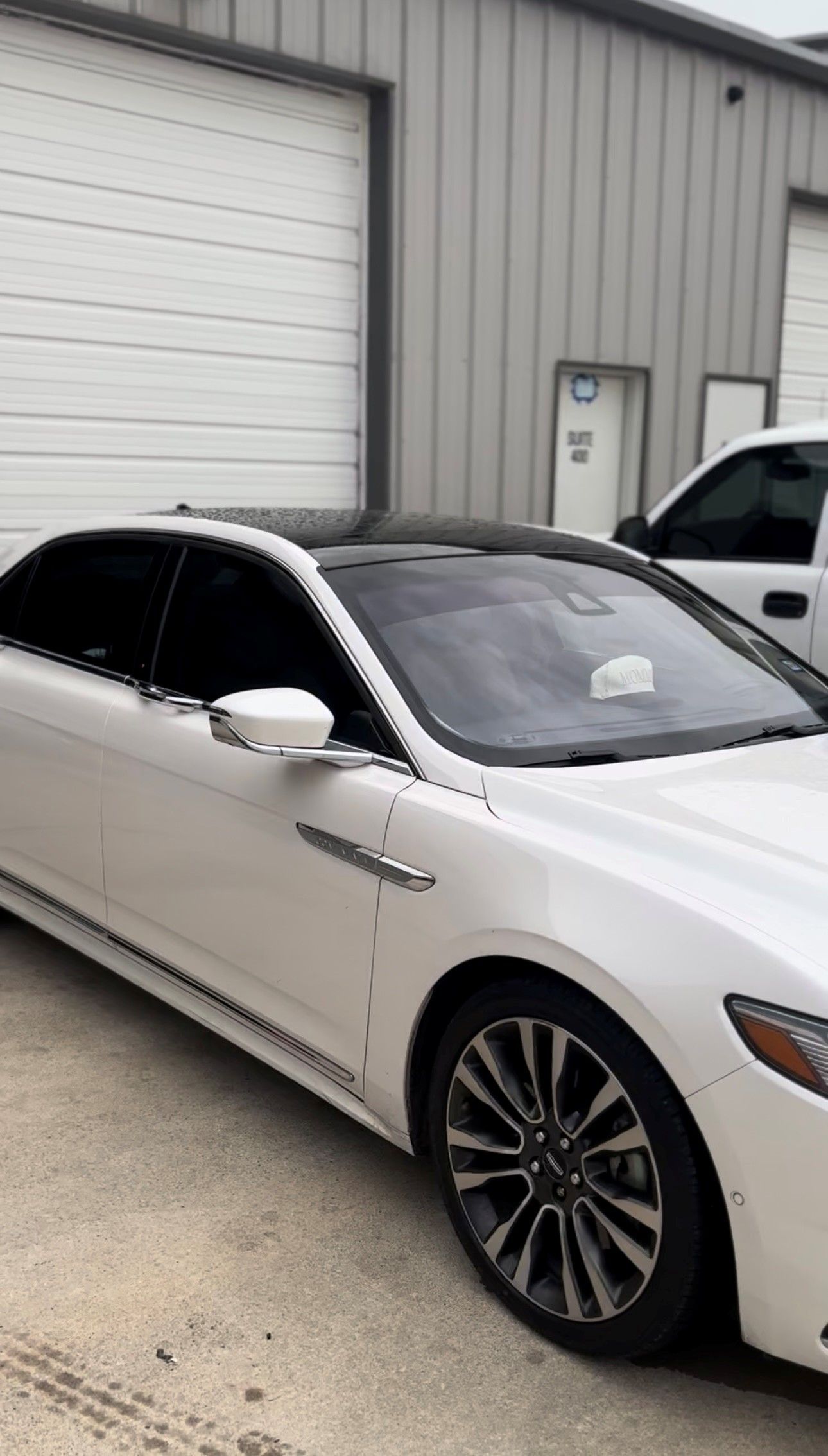 A white sedan with dark wheels and a sunroof parked in front of a gray metal building.