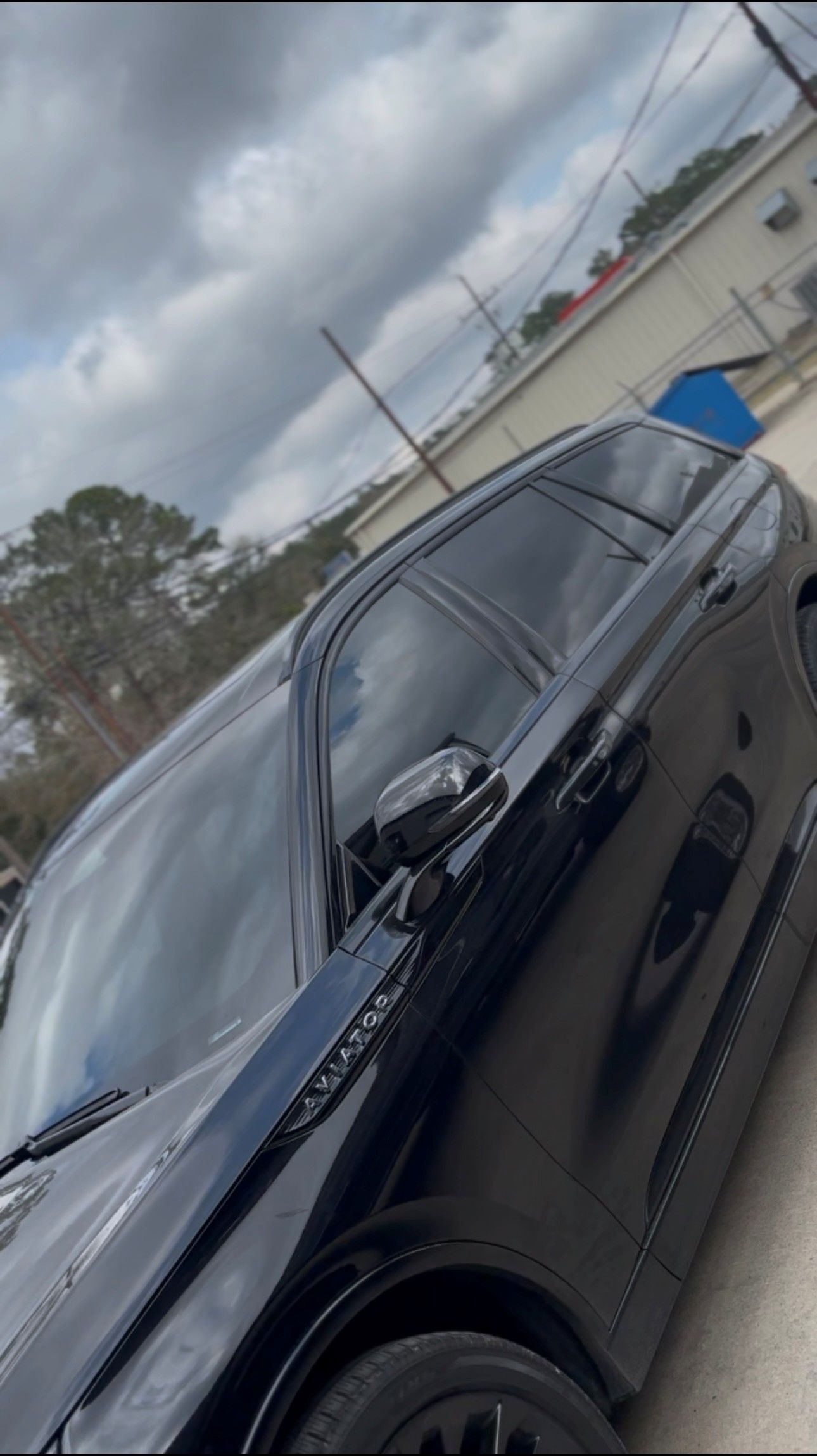A black SUV parked on an asphalt surface under a cloudy sky.