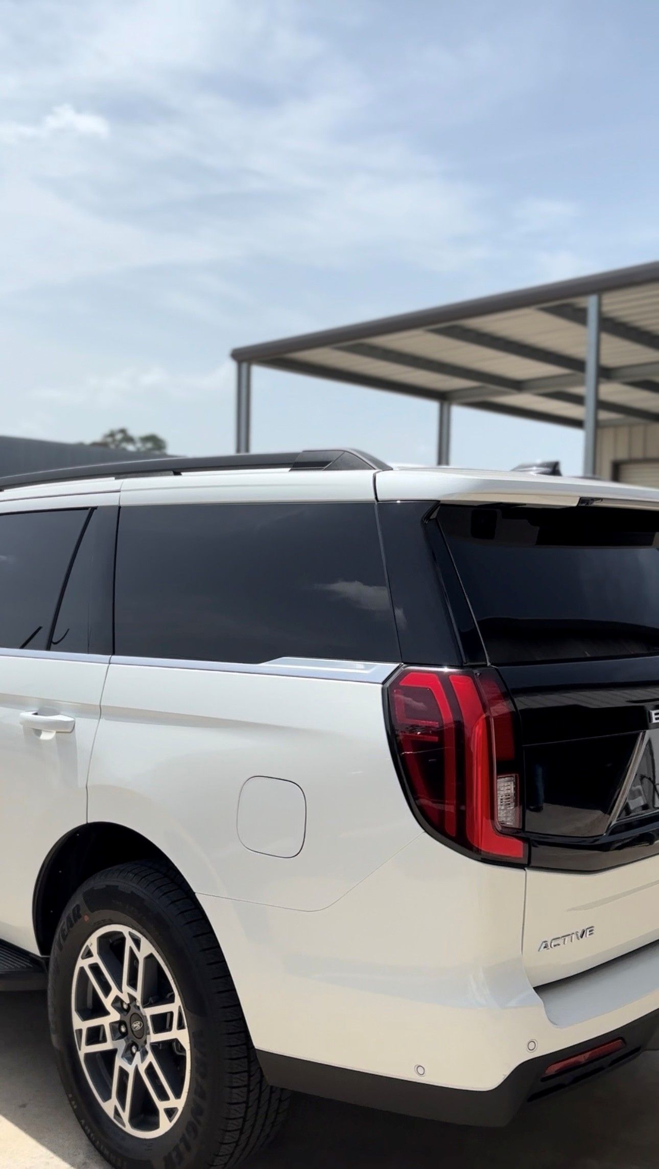 A white SUV parked outdoors under a metal structure, viewed from the rear quarter angle.
