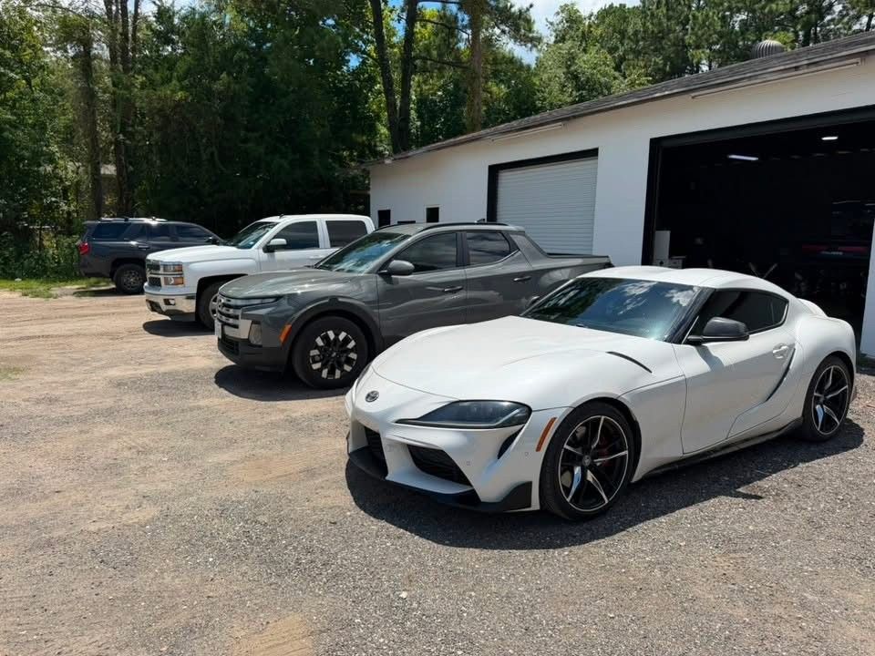 White sports car parked outside a garage with several other cars in a lot