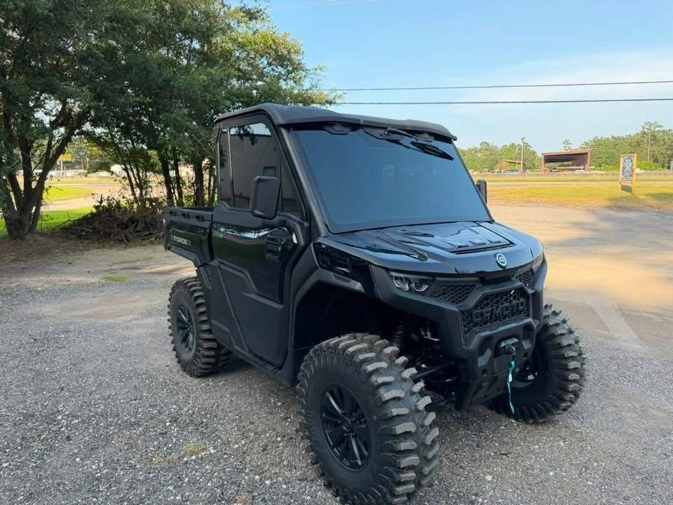 Black off-road UTV with large tires parked on gravel near trees and an open field.