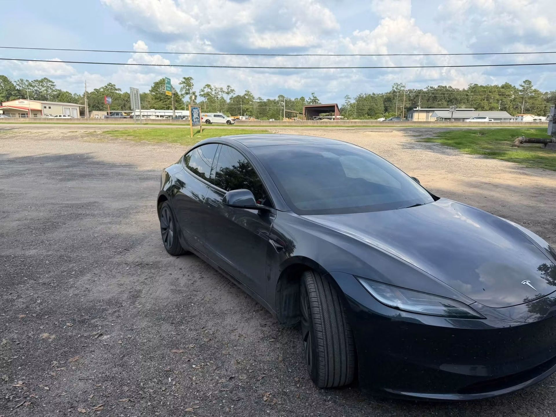 Black sedan parked on a gravel lot under a cloudy sky with one front wheel turned outward