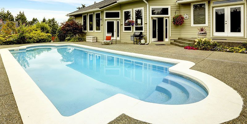 Backyard pool with steps, next to a light green house with windows and a door.