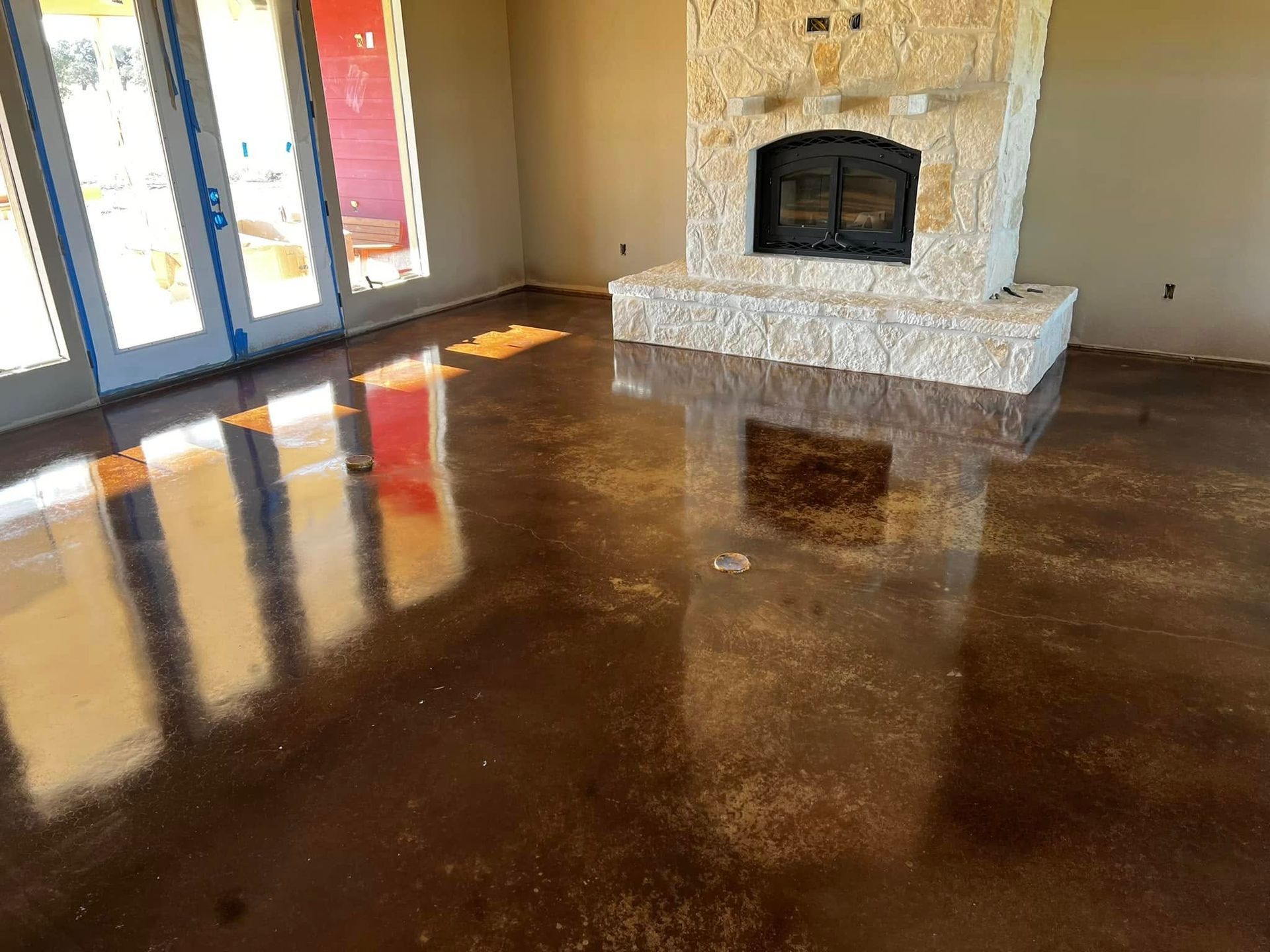 Shiny brown concrete floor with stone fireplace and French doors.