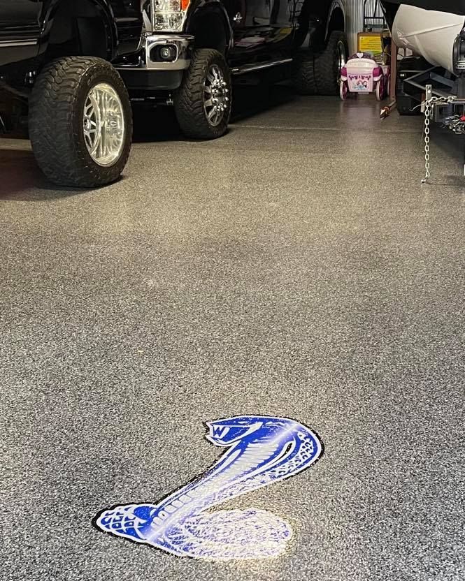 Garage floor with a blue and white cobra emblem, black truck parked, garage setting.