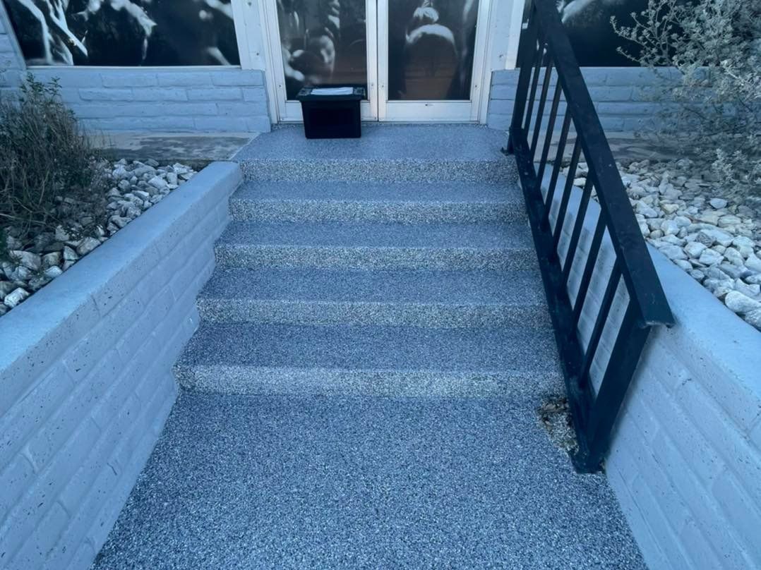 Exterior view of gray steps leading to a door with a black railing on the right.