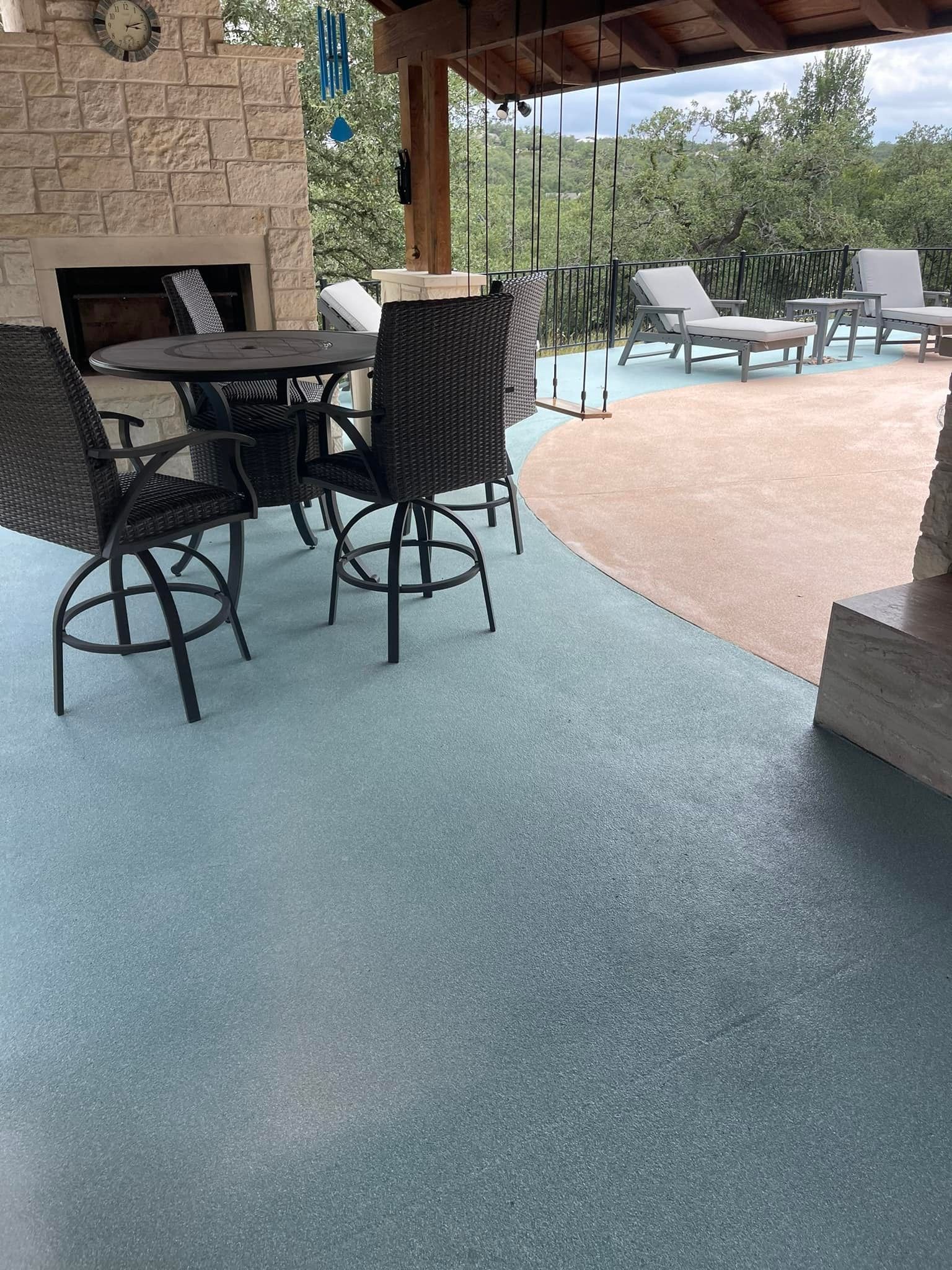 Outdoor patio with blue and tan speckled flooring, table, chairs, fireplace, and lounge chairs.