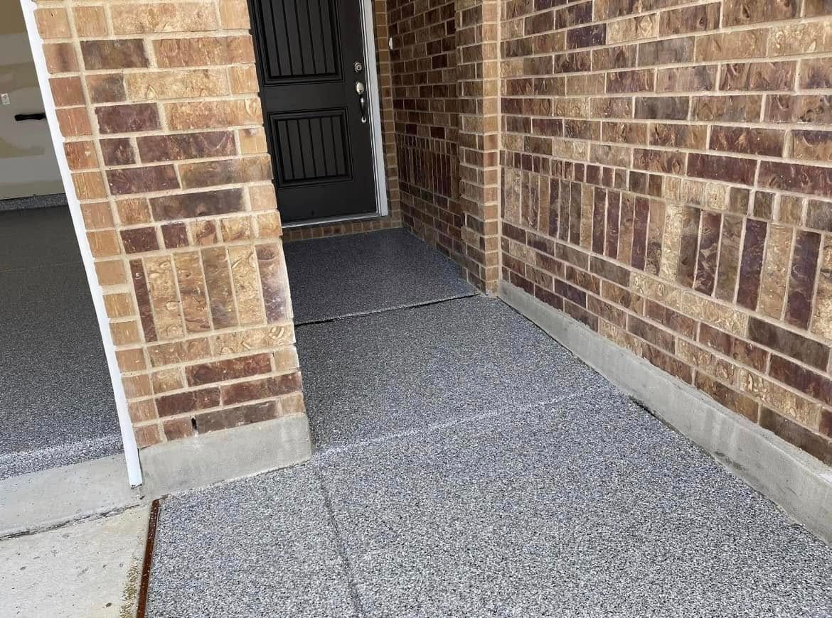Brick entryway with gray speckled flooring leading to a black door.