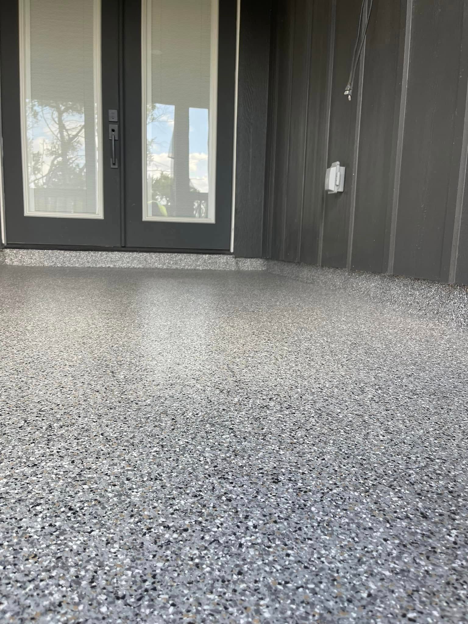Gray speckled epoxy floor in front of dark gray door and siding.